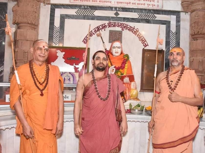 Three sannyasis with dandas standing before a garlanded statue of Adi Shankaracharya
