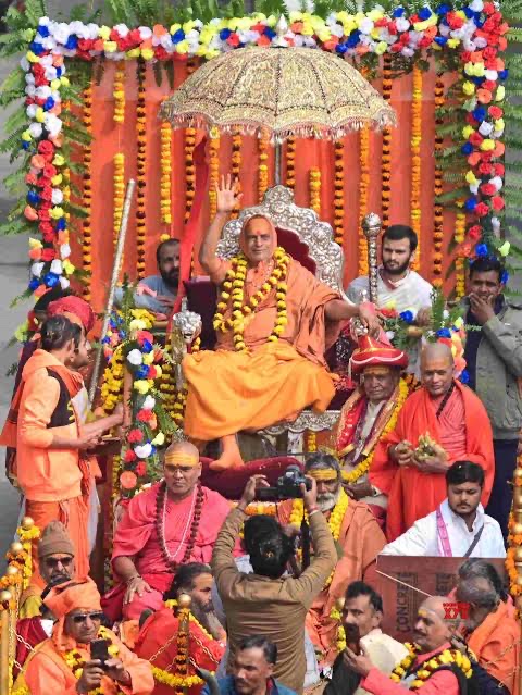 The Shankaracharya raising a hand in blessing from a silver throne beneath a gold parasol on a flower-decked float