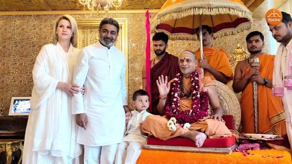 The Shankaracharya seated beneath a ceremonial parasol raising his hand in blessing to a visiting family with a small child, all dressed in white